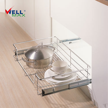 Referencing Kitchen drawer basket PTJ007E.jpg, the chrome 4-sided drawer basket is pulled out from a white cabinet on sliding tracks, neatly storing a stainless steel pot, stacked white plates, and a cup. Additionally, Kitchen drawer basket PTJ007E 1.jpg shows a close-up of the durable chrome wire construction situated next to a red cooking pan.