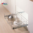 Referencing Kitchen drawer basket PTJ007H.jpg, the chrome 4-sided drawer basket is pulled out from a white cabinet on sliding tracks, neatly storing a stainless steel pot, stacked white plates, and a cup. Additionally, Kitchen drawer basket PTJ007H 1.jpg shows a close-up of the durable chrome wire construction situated next to a red cooking pan.