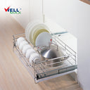 Referencing Kitchen drawer basket PTJ007V.jpg, the chrome drawer basket is pulled out from a white cabinet on sliding tracks, organizing white plates, bowls, and a stainless steel pot. Additionally, Kitchen drawer basket PTJ007V 1.jpg provides a detailed close-up of the polished chrome wire structure situated next to a red cooking pan.