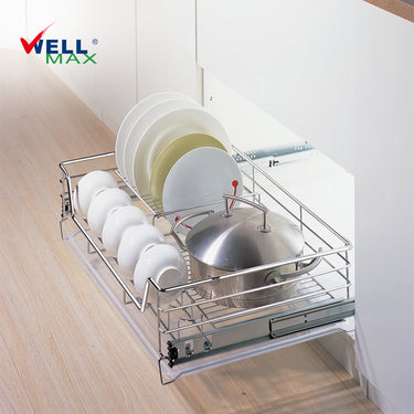 Referencing Kitchen drawer basket PTJ007V.jpg, the chrome drawer basket is pulled out from a white cabinet on sliding tracks, organizing white plates, bowls, and a stainless steel pot. Additionally, Kitchen drawer basket PTJ007V 1.jpg provides a detailed close-up of the polished chrome wire structure situated next to a red cooking pan.