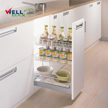 Referencing Soft-closing 3-layer pull out kitchen baskets PTJ004E5-150.jpg, a slim three-tier chrome wire pull-out basket is fully extended from a white kitchen base cabinet, neatly organizing tall seasoning bottles, stacked canned goods, and ceramic bowls on its distinct shelves.