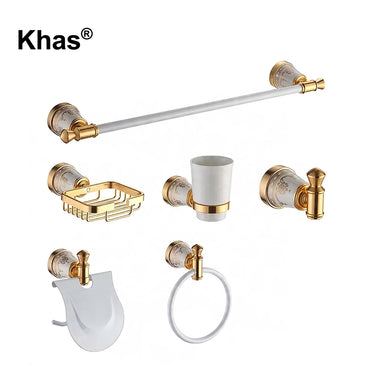 Referencing White and Gold Marble Type Bathroom Accessories Set 1.jpg, the complete Khas bathroom set—including a towel bar, soap dish, tumbler holder, robe hook, toilet paper holder, and towel ring—is displayed against a pristine white background, highlighting the white and gold marble finish. White and Gold Marble Type Bathroom Accessories Set 2.jpg shows the luxurious hardware fully installed in a warm, tiled bathroom setting, actively holding a towel, soap, and toothbrushes. White and Gold Marble Type B